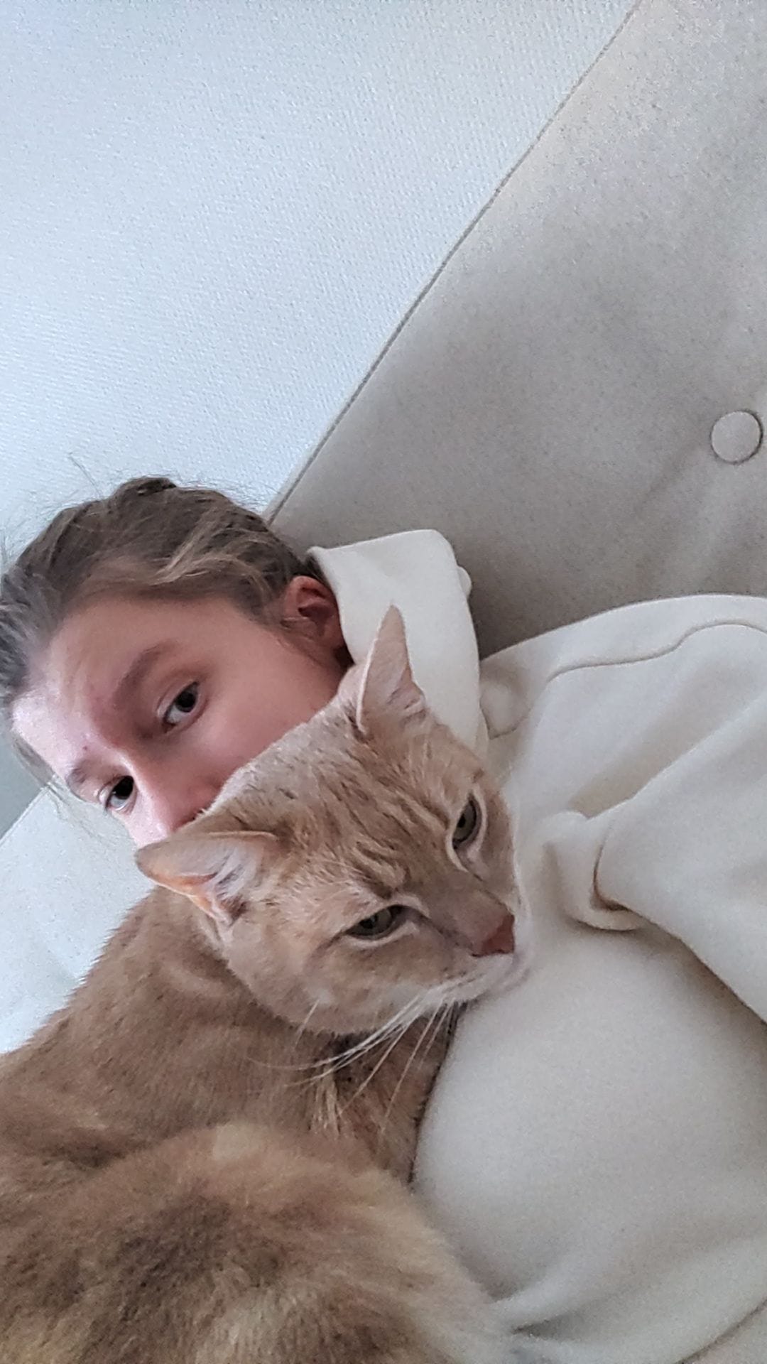 Kuvassa on Noora Carlson päällään valkoinen huppari. Hänen edessään makaa oranssi-valkoinen kissa.