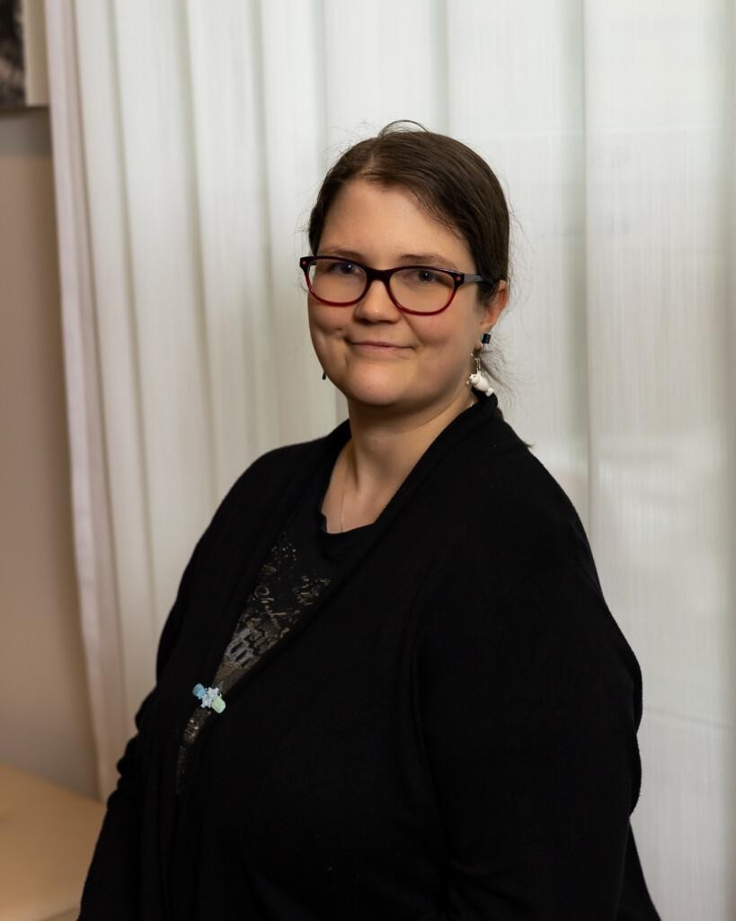 Kuvassa Sanna Larke. Sannalla on tummat hiukset, jotka ovat kiinni. Sannalla on tummasankaiset silmälasit ja musta neuletakki yllään.